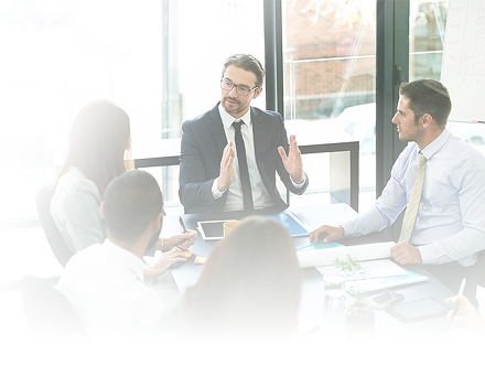 Four people in a meeting room looking at a colleague who is gesturing with his hands.