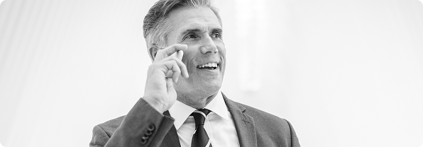 Professional in suit holding smartphone to ear during business call in bright modern setting.